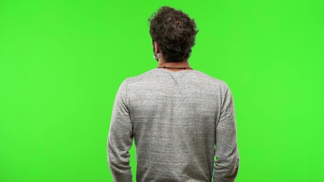 young man on chroma green screen from behind, looking back