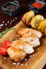 Roasted chicken breast and various vegetables on a chopping wood. With fried potatoes and meat sauces.