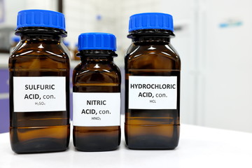 Selective focus of strong Nitric, Sulfuric and Hydrochloric acids in brown amber bottle. Blur white laboratory backdrop with copy space.