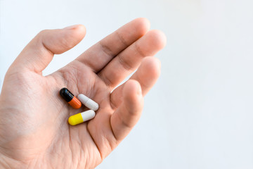 Three multi-colored pills in the form of capsules lie in an outstretched male hand