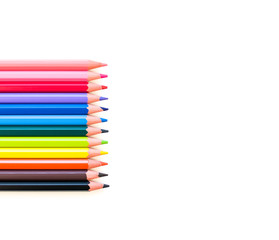 A set of colored pencils of all colors of the rainbow lies horizontally on the left in a row on a white background. Blank space on the right for text