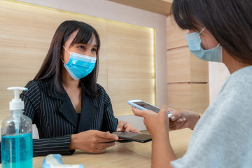 Receptionist and guest wearing face mask at front desk while having conversation in office or hospital . Covid 19 and coronavirus infection protection and protective policy concept .