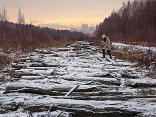 winter landscape with a girl in a field that stands on the trunks of felled trees covered with...