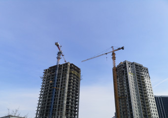 two tower cranes are building new houses from a monolithic frame and a monolithic-brick structure