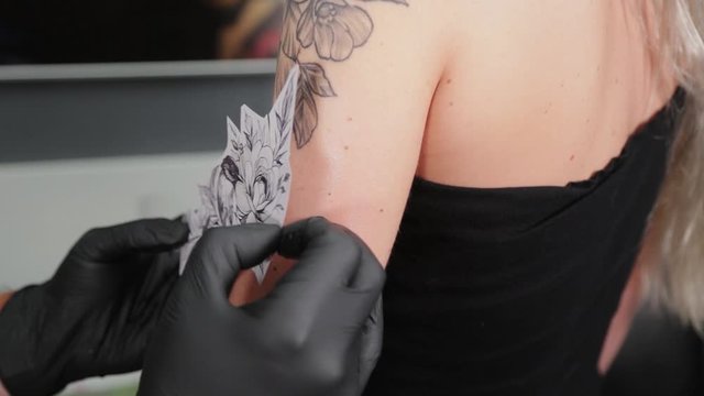 The tattooist glues a tattoo stencil to a girl's arm.