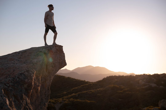 Young Man Standing On Ledge Overlooking Vast Landscape