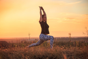 Girl practices yoga on a hill in nature during sunset or dawn