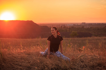 Fototapeta na wymiar Girl practices yoga on a hill in nature during sunset or dawn