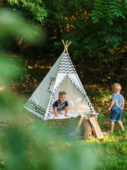 Two young boys playing in a backyard teepee campsite under the summer sunset