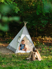 Young boy playing in a backyard teepee campsite under the summer sunset © Drew Woolery