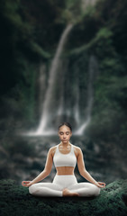 Beautiful young relaxed girl is engaged in yoga in the lotus position on the background of a waterfall in a tropical forest.