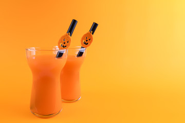 Halloween carbonated orange beverage in glass decorated with black tube and jack-o-lantern pumpkin on orange background. Homemade party Punch cocktail. Copy space