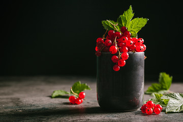 Red currant with leaves in a gray ceramic cup on a gray background.