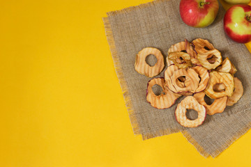 Natural apple chips on a burlap napkin on a yellow background. Healthy vegan vegetarian fruit snacks. Organic products for wellness.