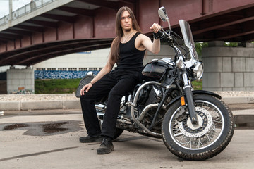 Naklejka na ściany i meble Long-haired guy on a black motorcycle under the bridge