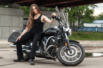 Obraz na płótnie Canvas Long-haired guy on a black motorcycle under the bridge