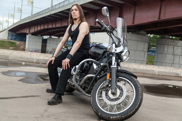 Fototapeta na wymiar Long-haired guy on a black motorcycle under the bridge