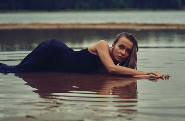 Fototapeta premium lying girl in a long black dress on the shore of the bay, the concept of the joy of health, sleep and relaxation 