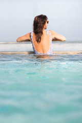 Pretty young woman out of focus in a flower-backed swimsuit in a pool. Focus on the water.