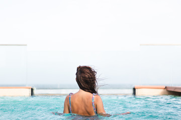 Nice young woman in a flowered bathing suit looking at the horizon from a swimming pool. Landscaped photography.