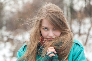 Girl with long blond hair in a turquoise jacket with a bright scarf in a winter park