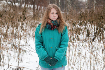 Girl with long blond hair in a turquoise jacket with a bright scarf in a winter park