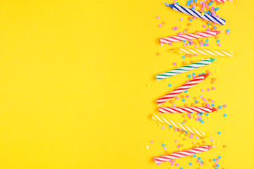 Birthday cake candles with candy sprinkles. Overhead view side border on a yellow background. Copy...