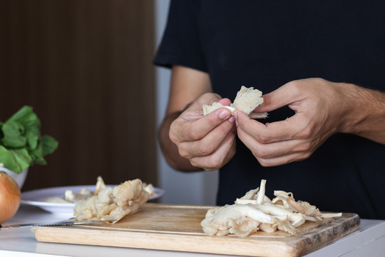 Closeup shot of a cutting board and a young man cutting  oyster mushrooms