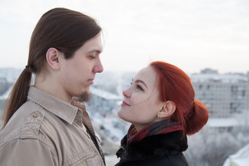 Long haired guy and red haired girl huging on snowy rooftop
