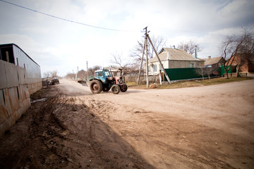 Fototapeta na wymiar Tractor drives along rural street in spring