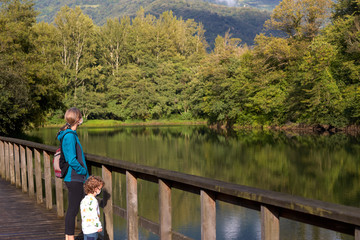 mother and son on a bridge over a lake looking at the landscape with protection mask