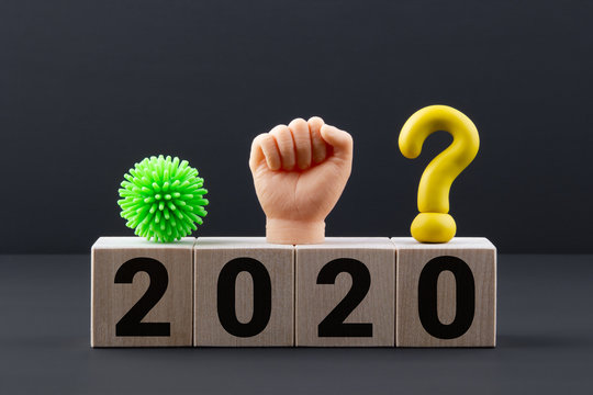 Text 2020 on wooden blocks with question mark, the symbol of the coronavirus and a toy hand clenched into a fist. Business concept of predicting the future after pandemic and protests in the world.