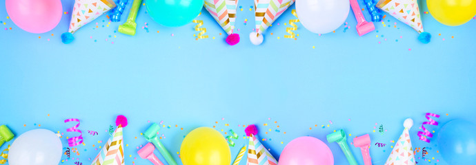 Birthday party banner with double border on a blue background. Top down view with confetti, balloons, party hats and streamers. Copy space.