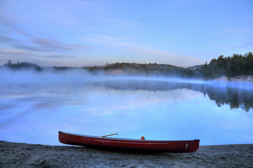 Canoe on shore of George Lake with shoreline in mist Killarney Park Ontario Canada