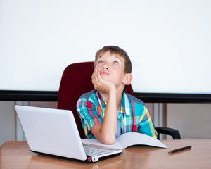 A cute boy sits at the table, looks up, remembers his homework. The boy didn't learn his homework, Copy space