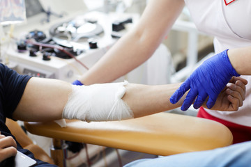 Close-up of patient with bandaged hand donating blood with nurse working with him