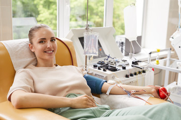 Portrait of young woman smiling at camera while lying on the couch and donating the blood at hospital - obrazy, fototapety, plakaty