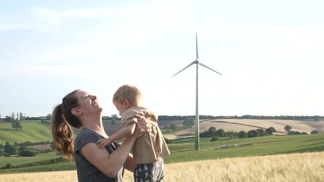 Happy mother plays with her son in a field with a wind turbine in the background on a beautiful summer day