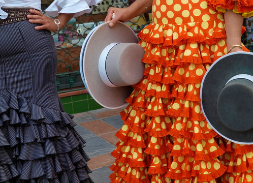 Dos mujeres vestidas con traje de flamenca sostienen en sus manos los tipicos sombreros andaluces