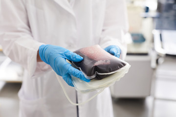 Close-up of doctor in protective gloves and in white coat holding package with blood at hospital