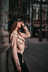 Fototapeta premium beautiful model in a black hat and beige jacket poses near a lamppost . city background 