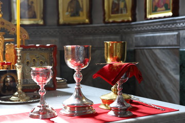 Metal, silver and gold bowls for communion, covered with red cloth on the throne. Part of the liturgy in the Orthodox Church. Against the background of Orthodox icons.