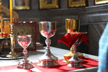 Metal, silver and gold bowls for communion, covered with red cloth on the throne. Part of the liturgy in the Orthodox Church. Against the background of Orthodox icons.