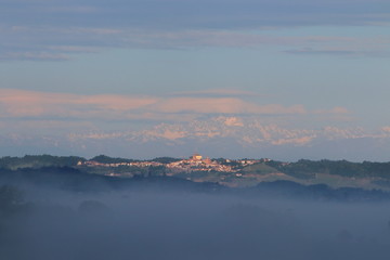 A view of the Monferrato Astigiano hills shrouded in thick fog with the snowy Alps in the background.