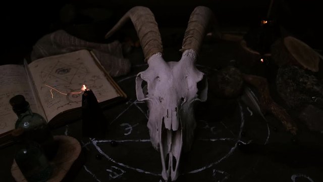 White goat scull with horns, open old book, runes, black candles on witch table. Occult, esoteric, divination and wicca concept. Halloween concept.
