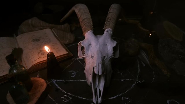 White goat scull with horns, open old book with magic spells, runes, black candles on witch table. Occult, esoteric, divination and wicca concept. Halloween and Day of the dead concept. 
