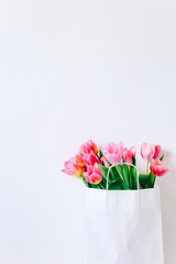 Fresh pink tulip flowers in paper bag on white wall background