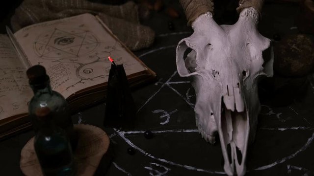 White goat scull with horns, open old book, runes, black candles on witch table. Occult, esoteric, divination and wicca concept. Halloween concept.