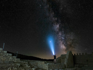 A stargazer lights up Saturn with his powerful flashlight. The Milky Way Galaxy is above him and...