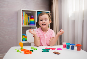 cheerful little girl playing with plasticine at the table in the room